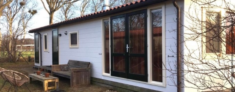 Een wit chalet met een houten tuinset ervoor