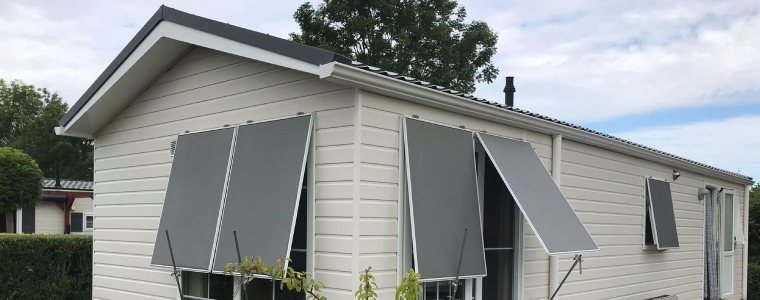 Een schuin aanzicht van een wit chalet compleet gerenoveerd met grijze zonwering voor de ramen