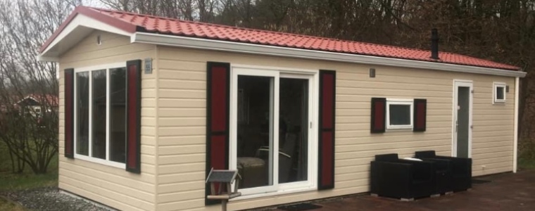 De kosten voor het renoveren van een chalet zijn deels afhankelijk van de werkzaamheden. Een schuinaanzicht van een cremekleurig chalet met rode luikjes en een rood pannendak