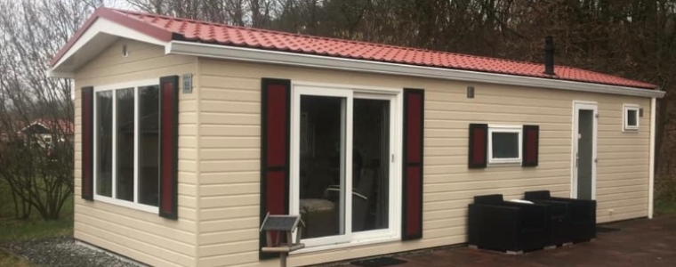 Een schuinaanzicht van een cremekleurig chalet met rode luikjes en een rood pannendak